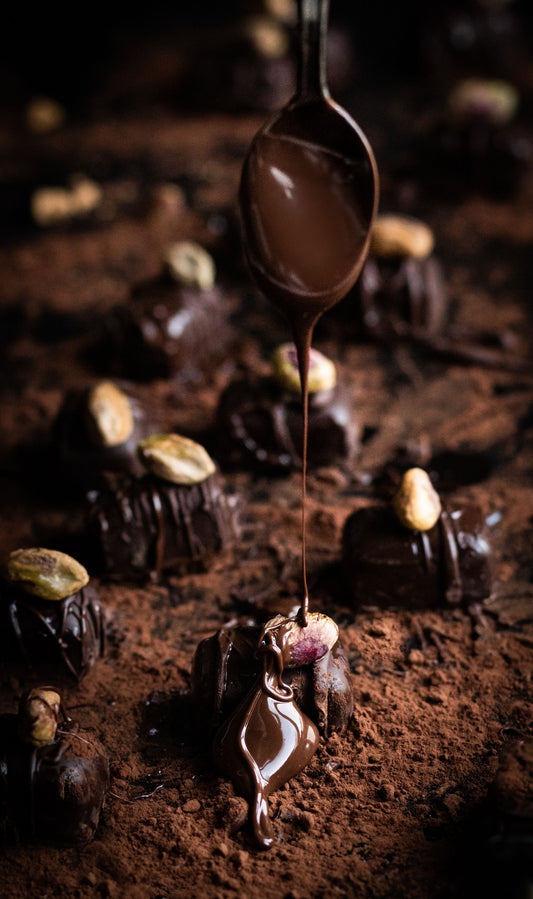 Chocolate being spooned over pistachio-topped sweets — pistachio stuffed dates, the viral no-bake Dubai dessert